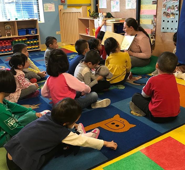 Adult reading a book to a group of children in a classroom