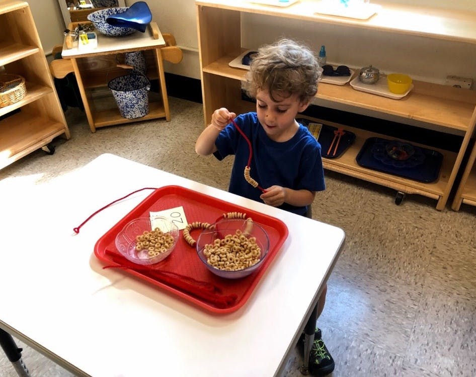 Child stringing beads onto a red string at a table