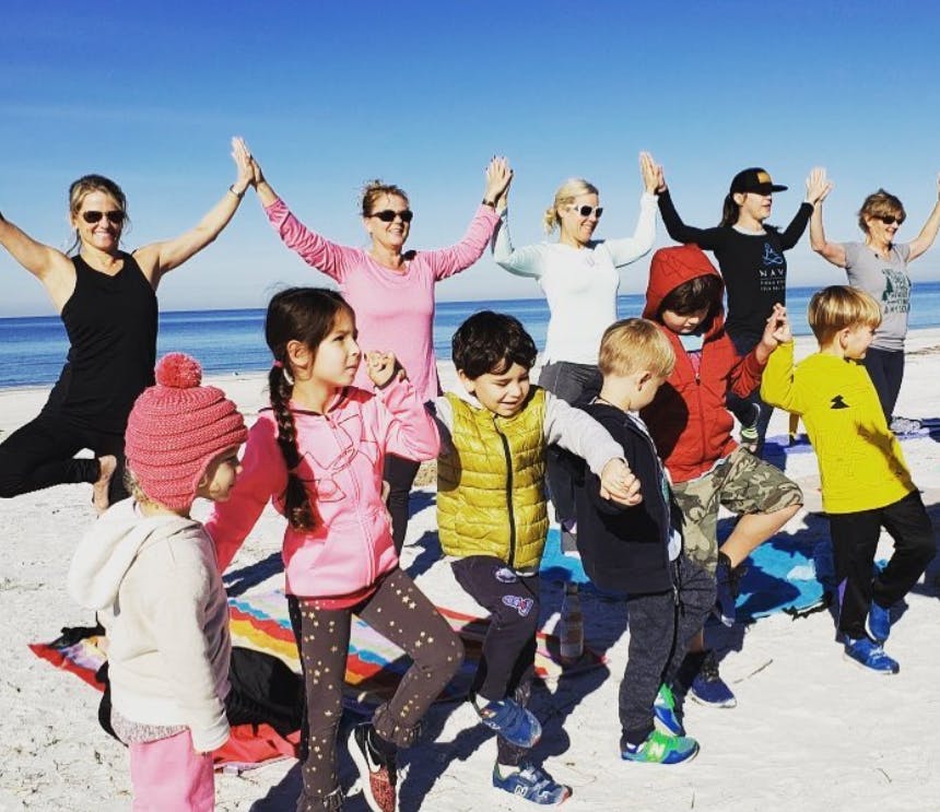 Adults and children doing yoga poses on a beach