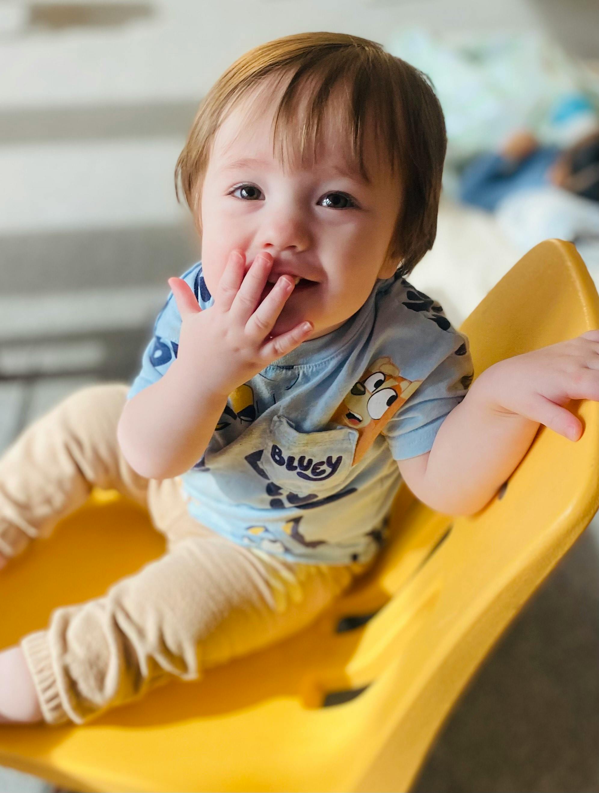 Child sitting in a yellow chair with a hand over their mouth