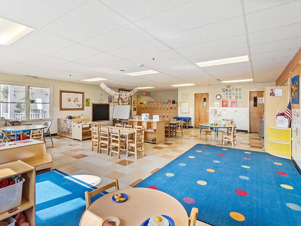 Classroom with small tables and chairs, shelves, and a blue rug