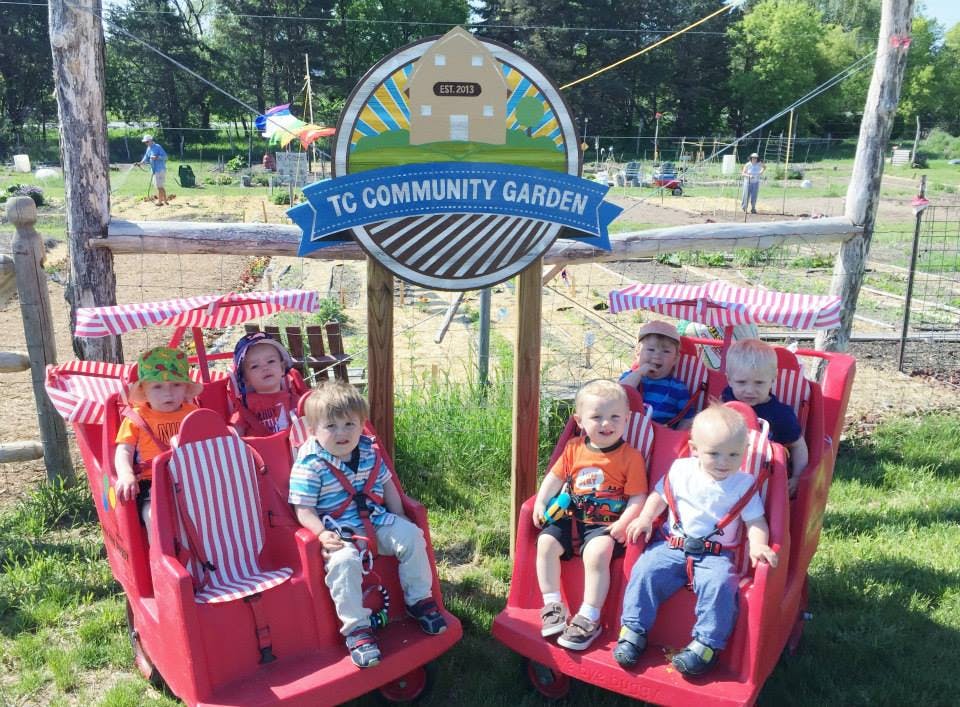 Children in red wagons with a "TC Community Garden" sign