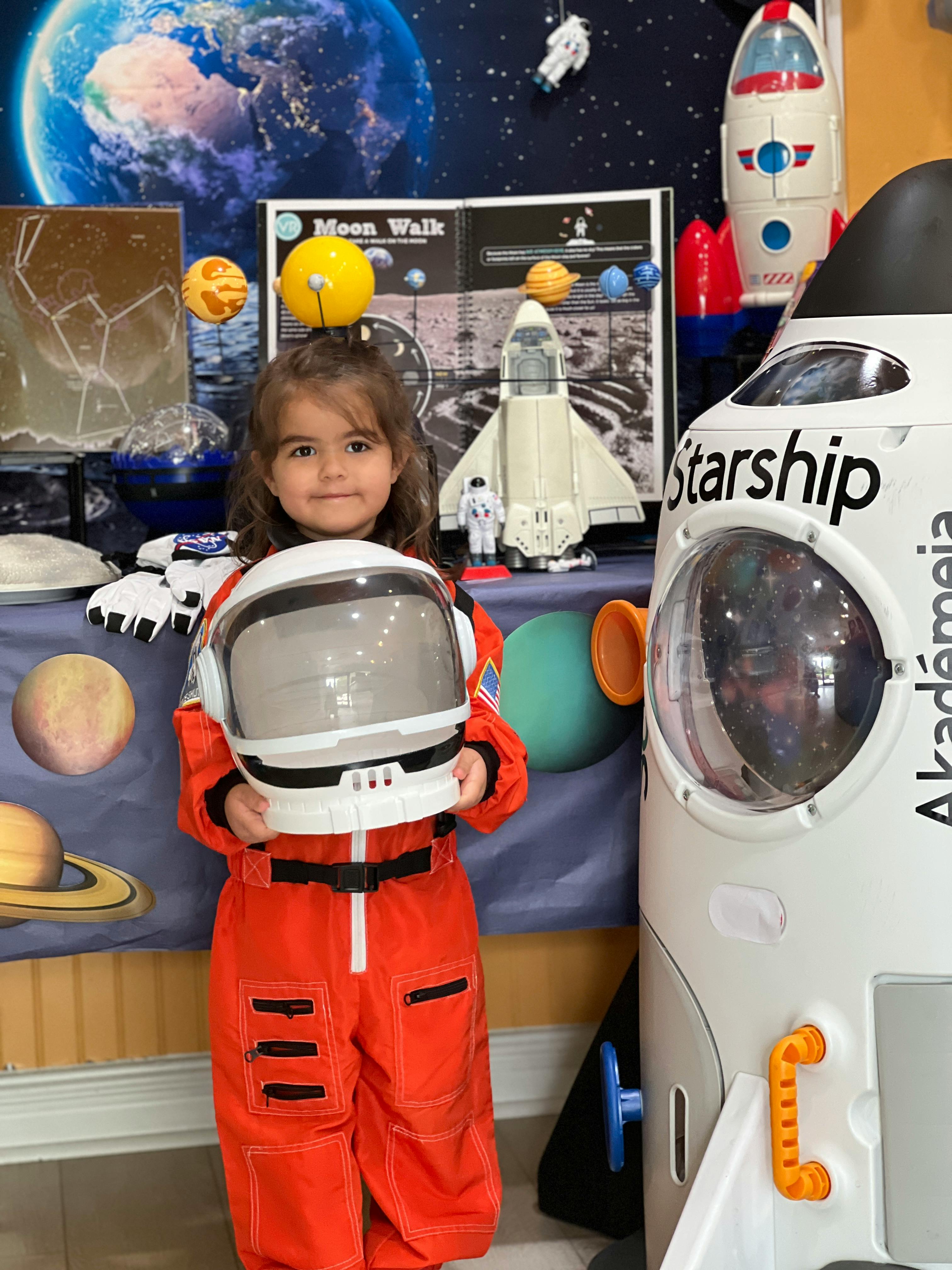 Child in an orange astronaut suit holding a white astronaut helmet