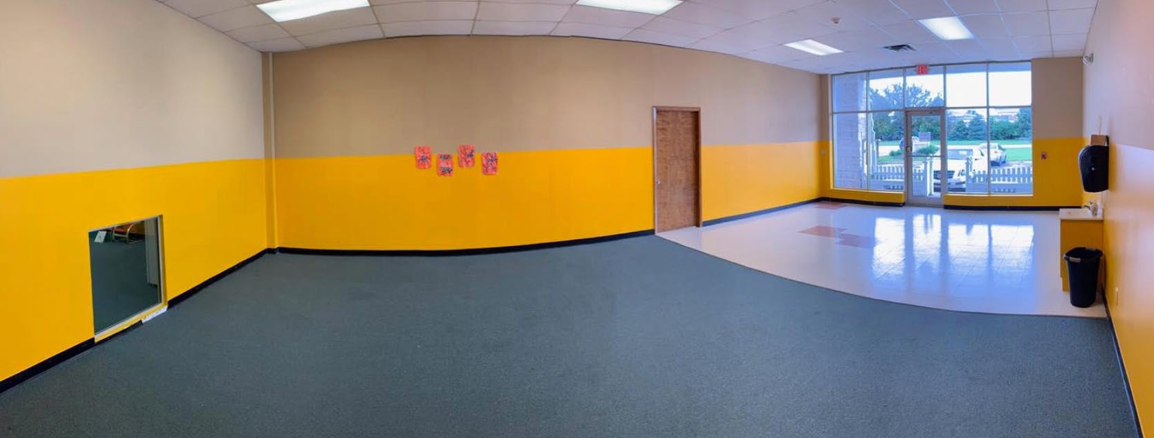 Empty room with yellow and beige walls, dark floor, and large windows