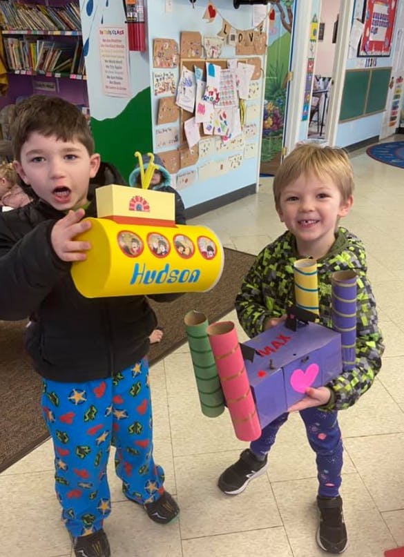 Two children holding handmade crafts in a classroom