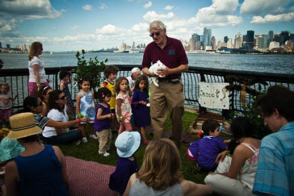 Adult holding a small animal for a group of children and adults outdoors