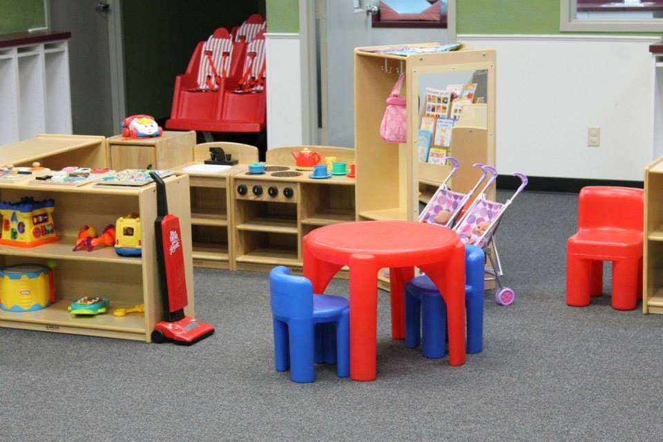 Playroom with toy kitchen, shelves of toys, and small red table with blue chairs