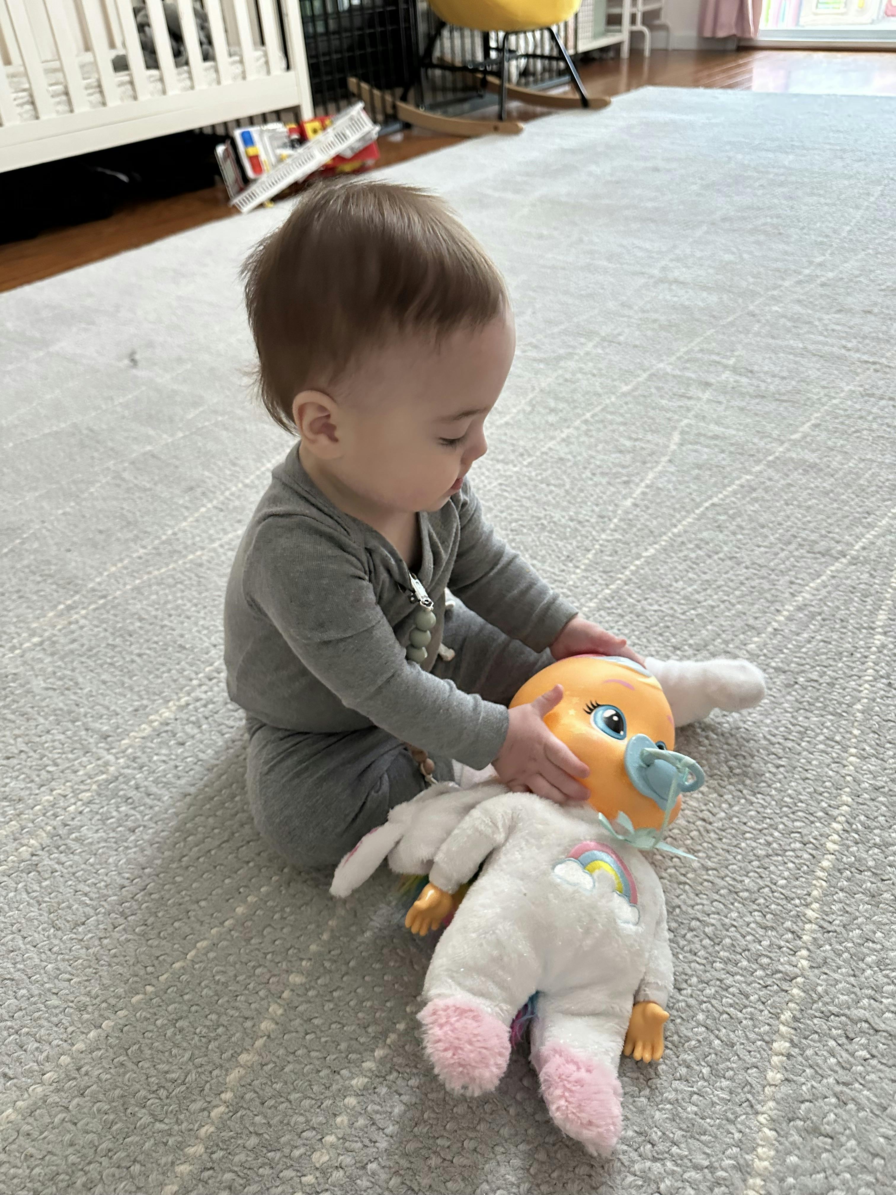 Child sitting on floor, playing with a doll wearing a unicorn outfit