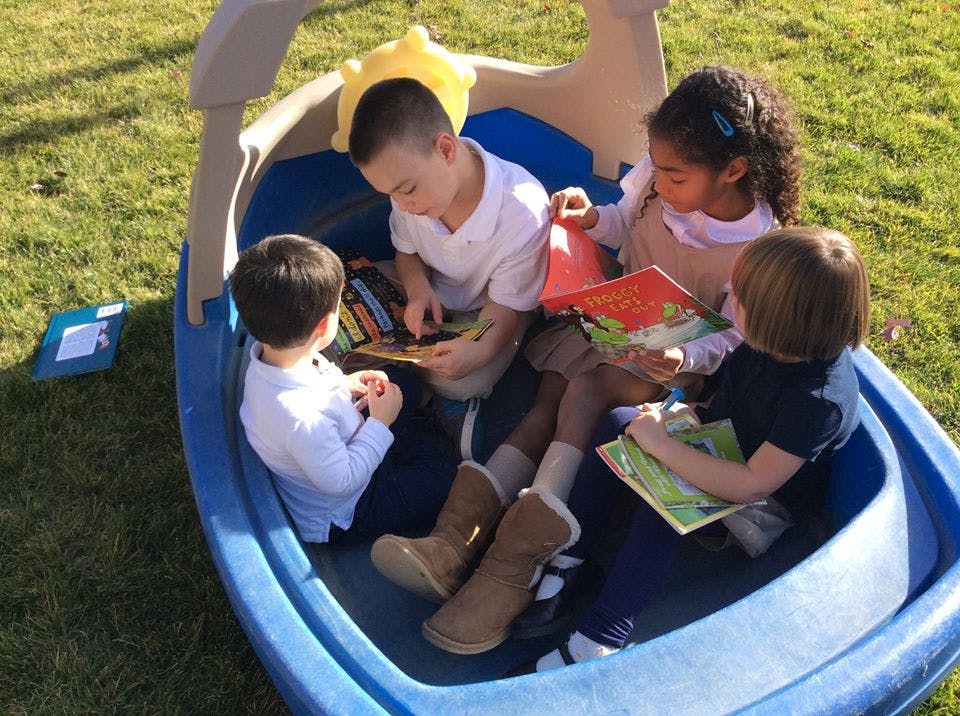Four children sitting in a blue play boat reading books