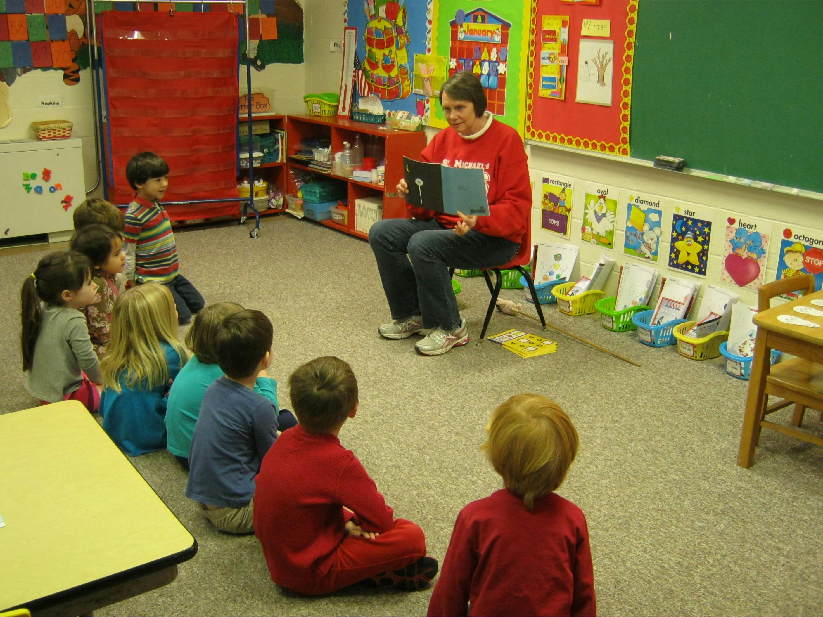 Person reading a book to a group of children in a classroom
