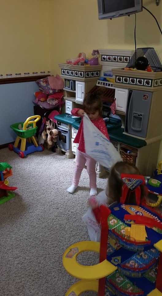 Child holding a white cloth in a room with toys