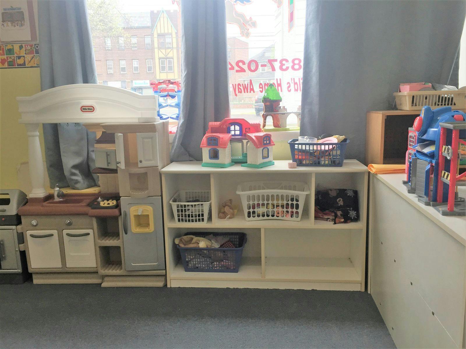 Play kitchen and shelves with toys in a room with window in background