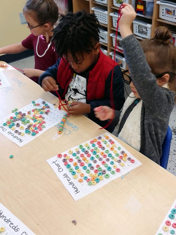 Children stringing cereal onto yarn at a table