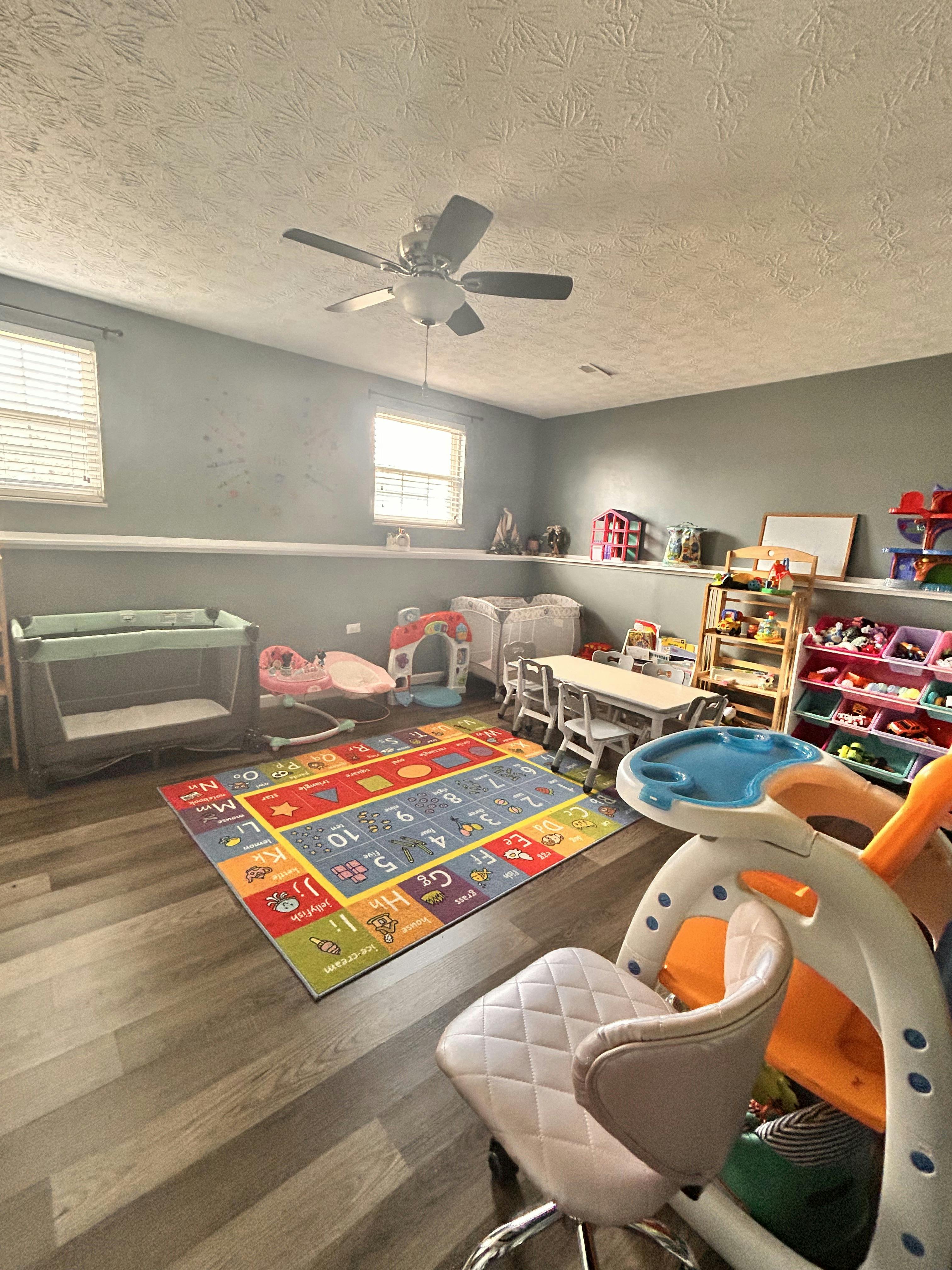 Playroom with colorful rug, crib, small table and chairs, and toy shelves