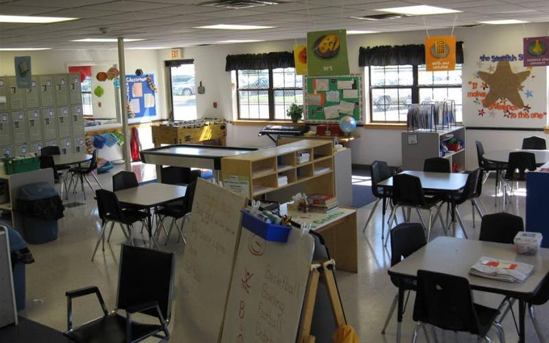 An empty classroom with small tables, chairs, lockers, and games