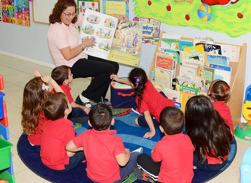 Person reading a large book to a group of children in a classroom