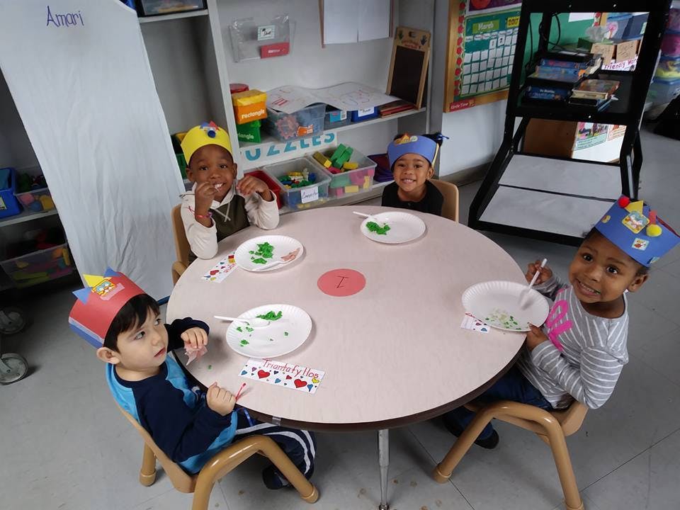 Four children wearing paper crowns sitting at a table in a classroom