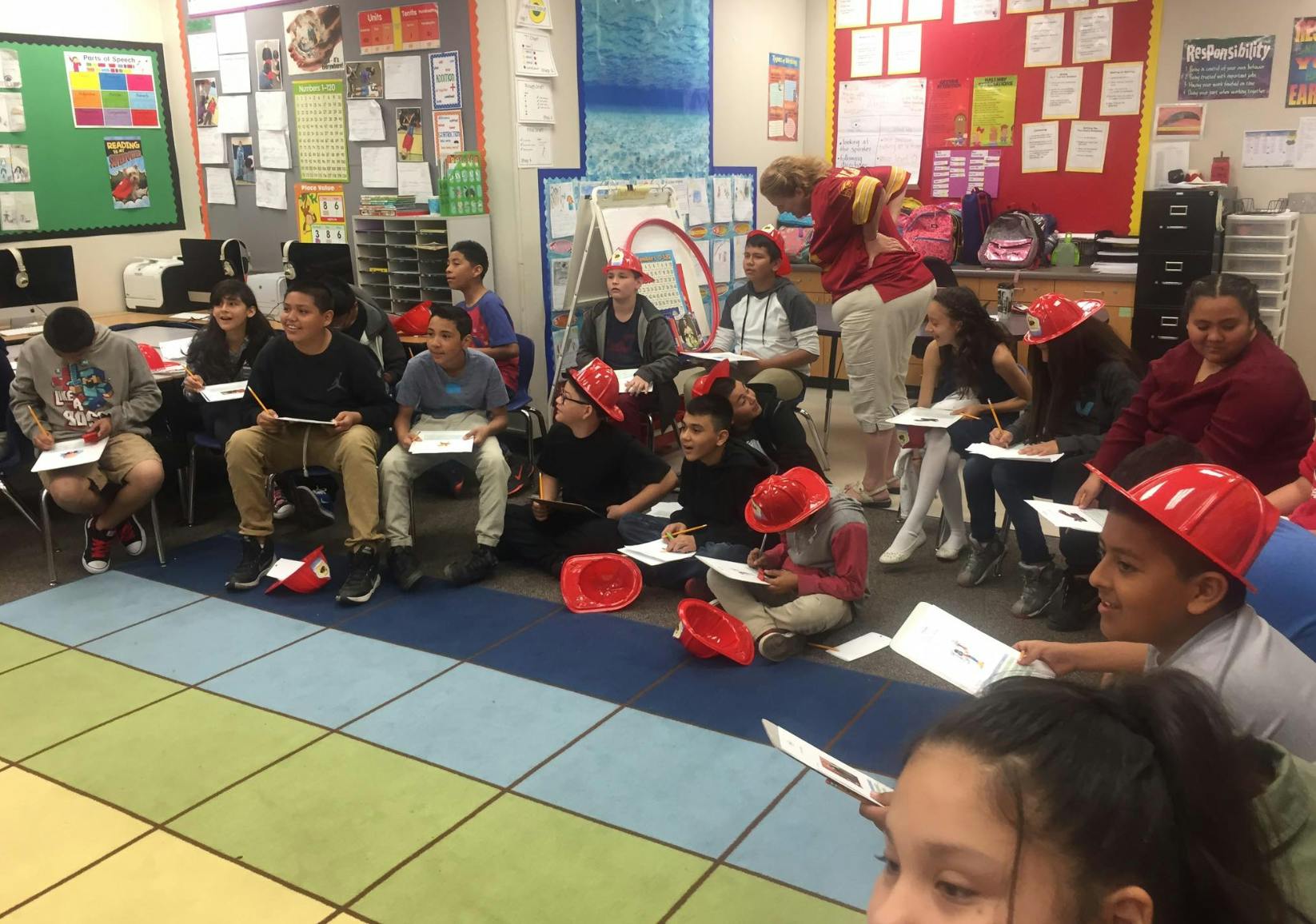 Children and teens in a classroom, some wearing red hats, writing on paper
