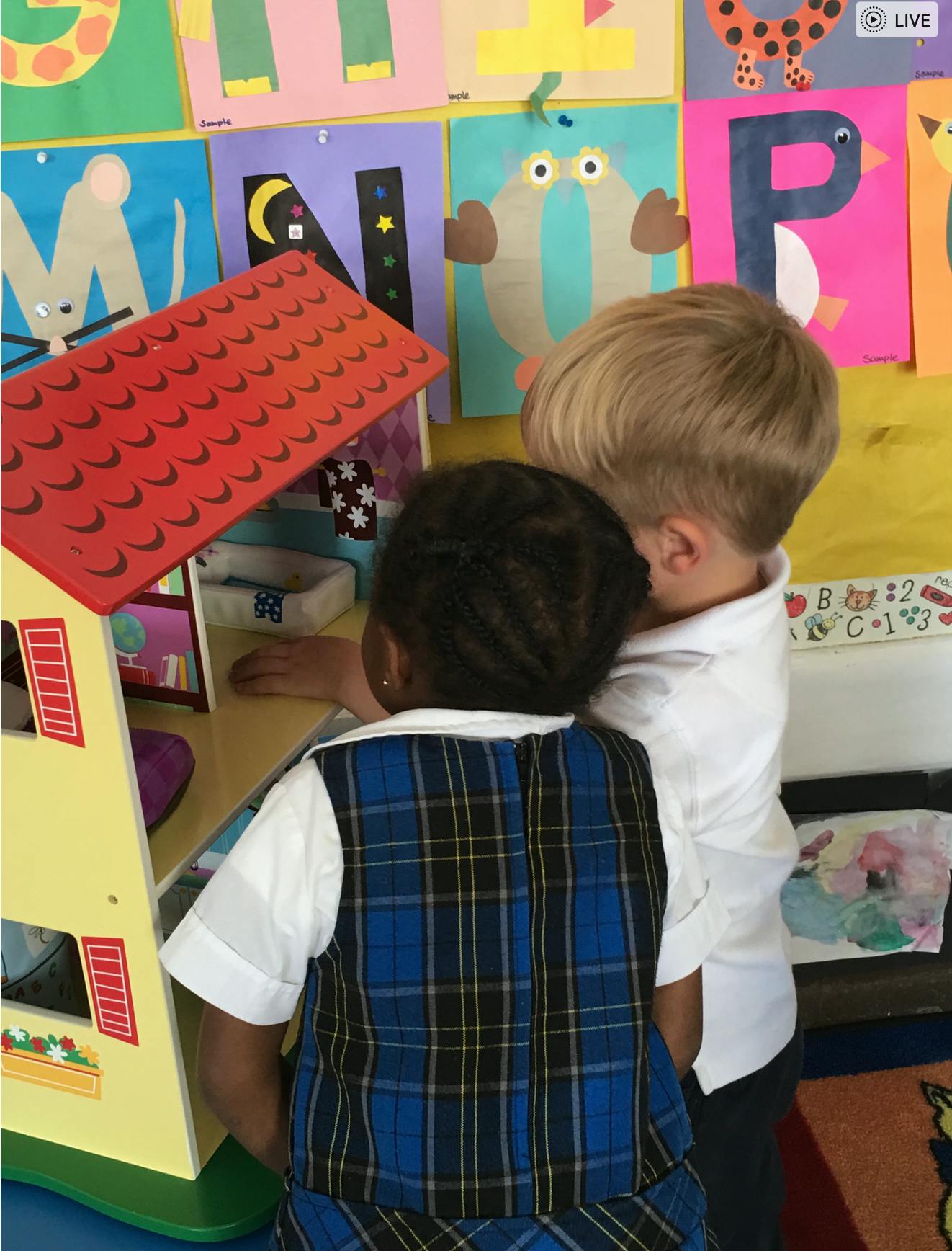 Two children playing with a dollhouse in a classroom