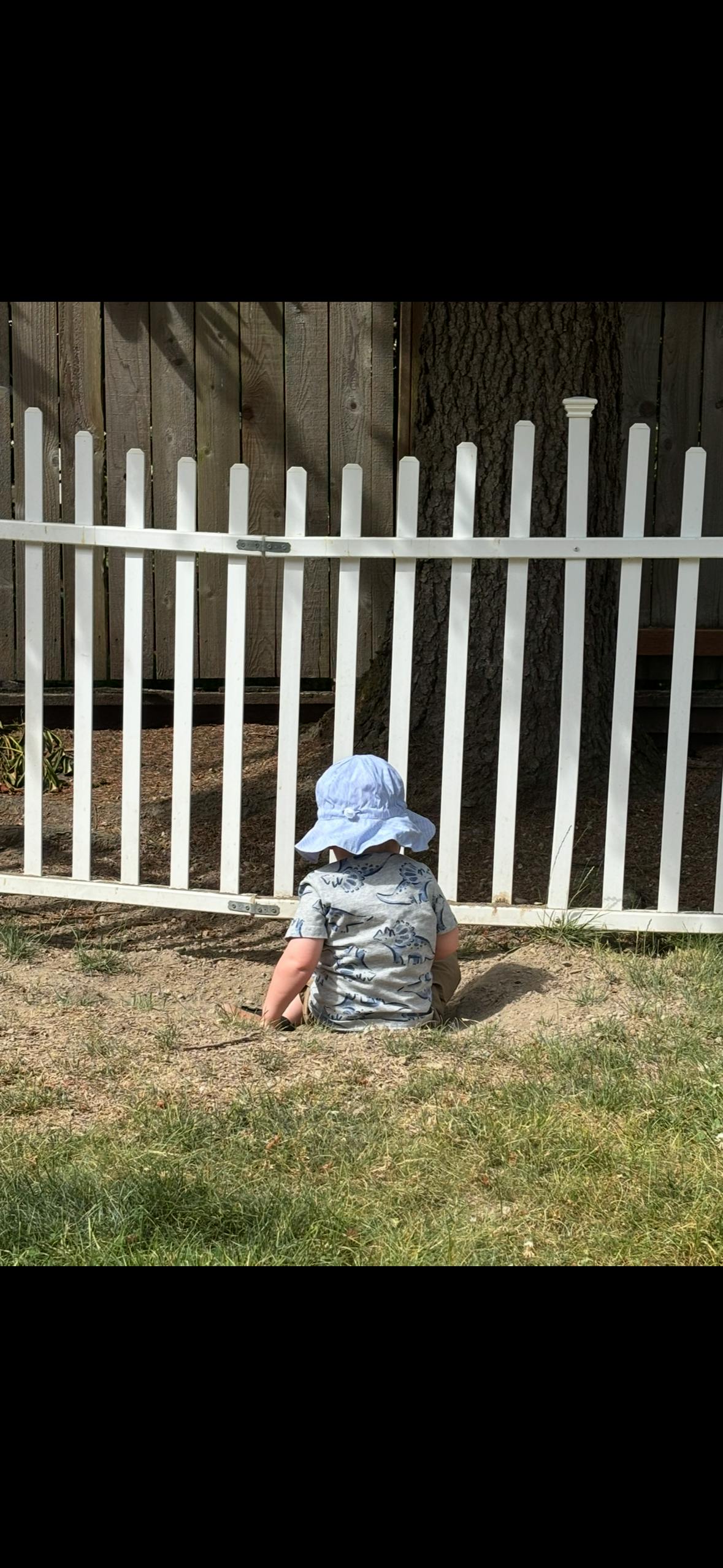 Child sitting on the ground by a white fence
