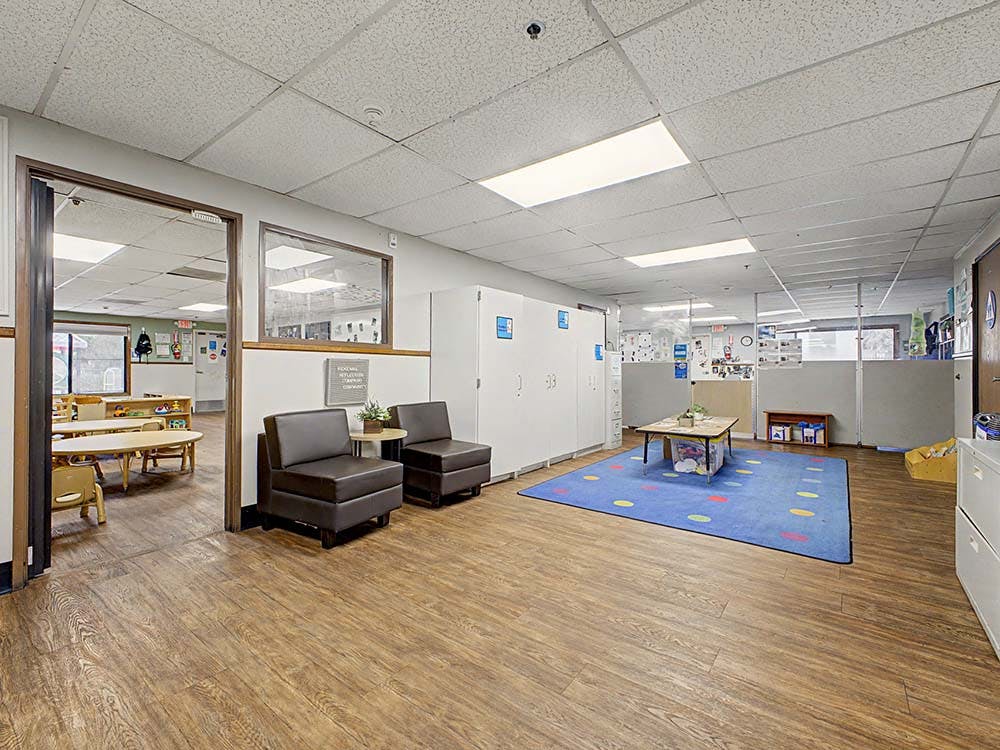 Child care classroom with tables, chairs, and colorful rug
