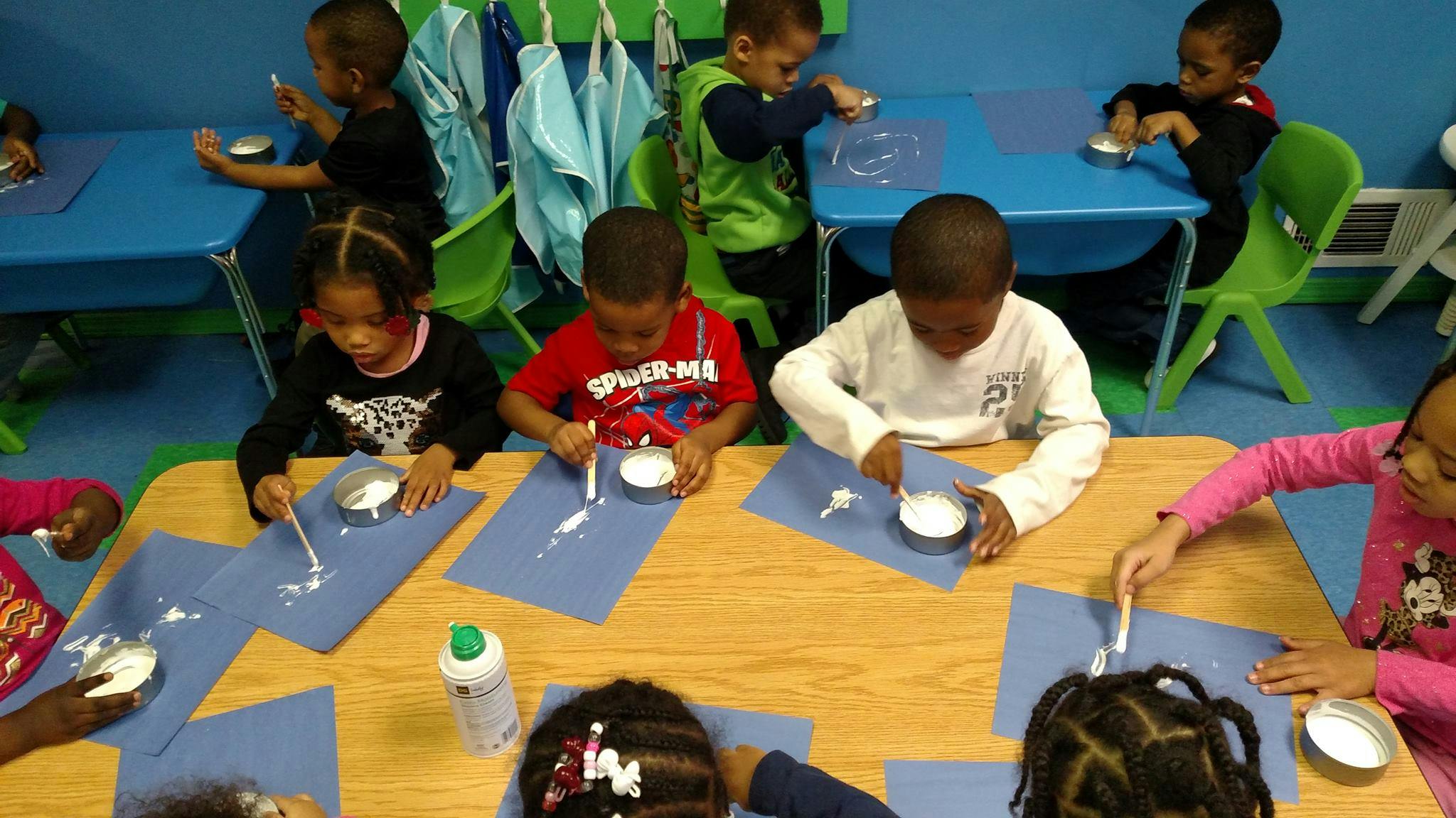 Children at tables doing an art activity with white paste on blue paper