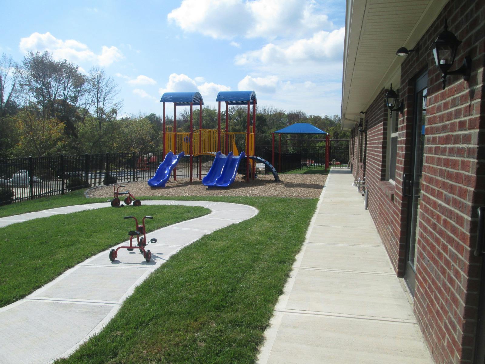 Playground with slides and tricycles on a winding path next to a brick building