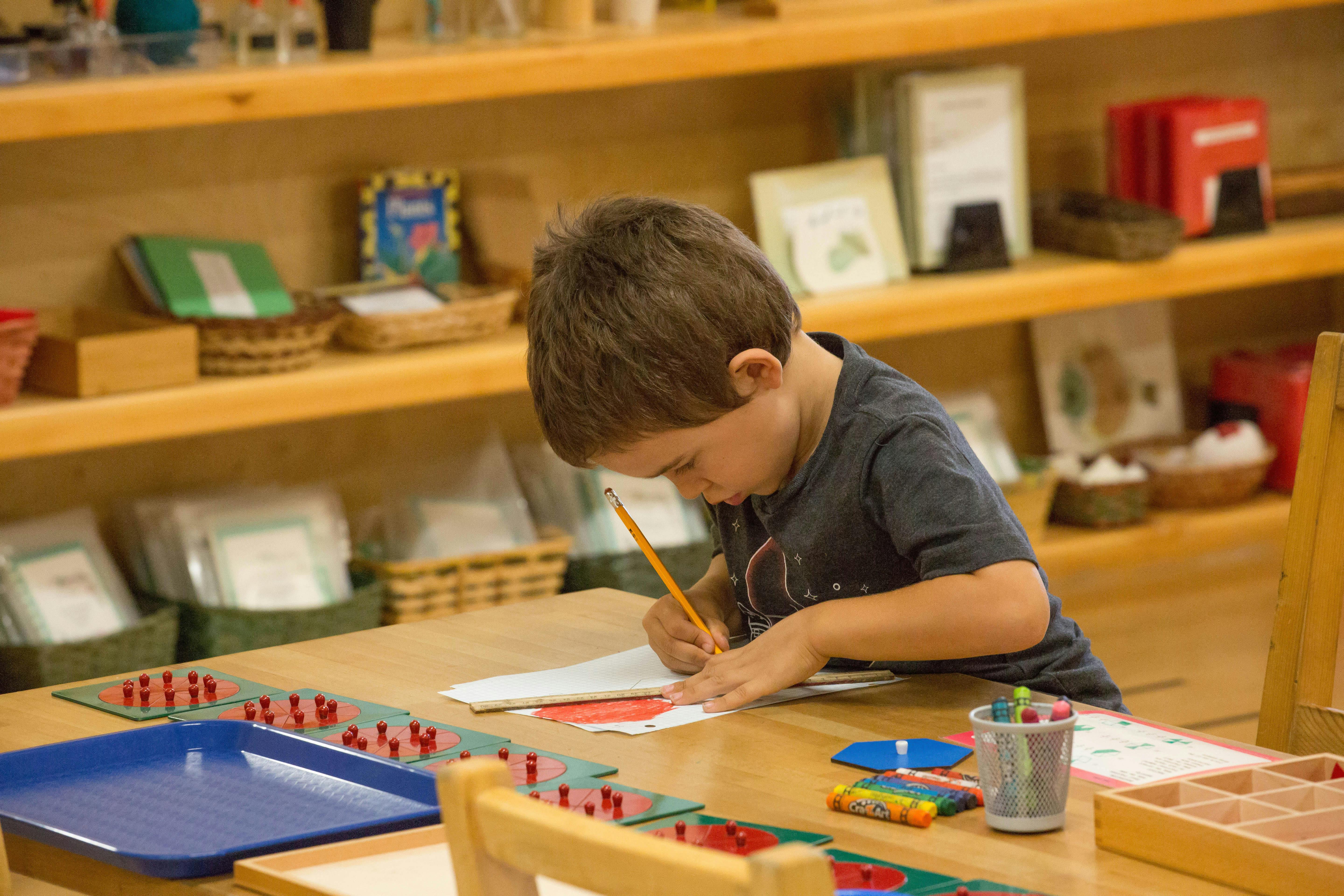 Child writing with a pencil at a table in a classroom