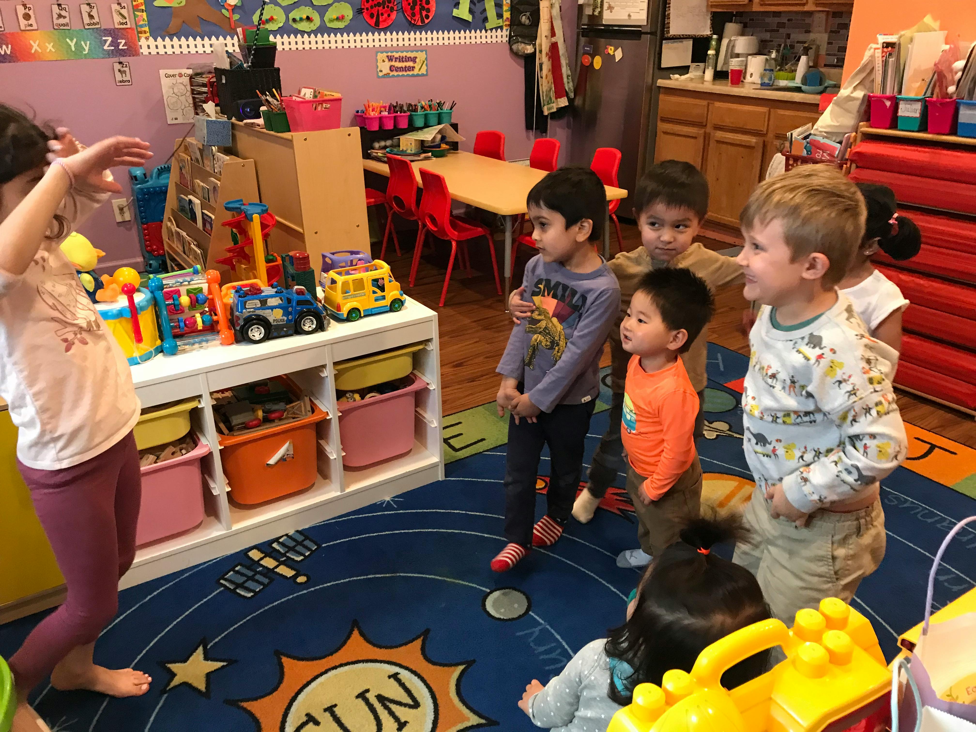 Children gathered in a classroom, some looking at toys on a shelf