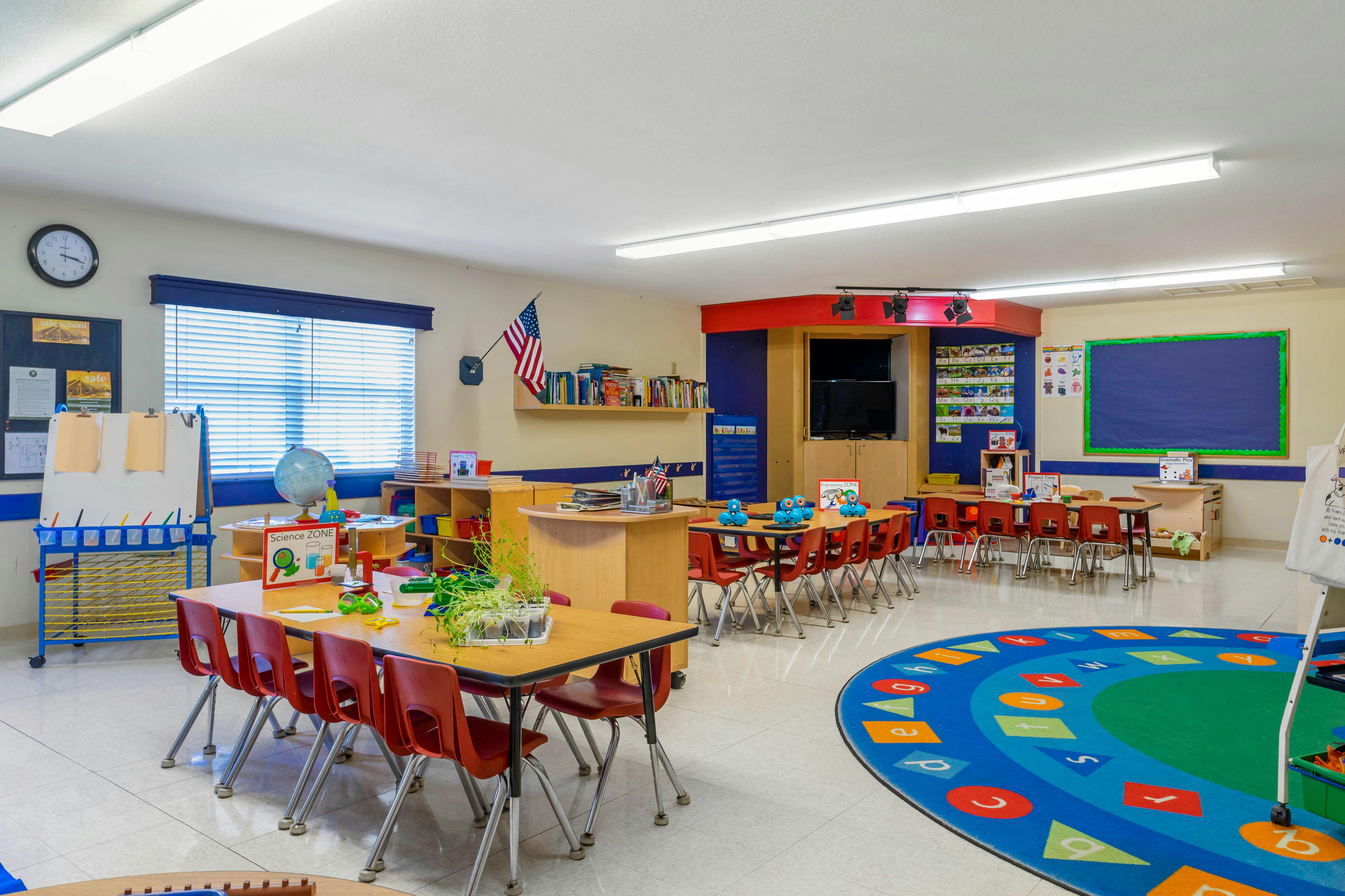 Classroom with tables, chairs, teaching aids, and a colorful rug