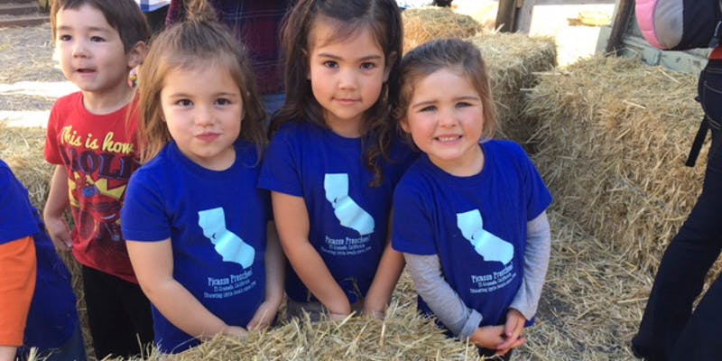 Three children in blue shirts with a California logo standing in hay