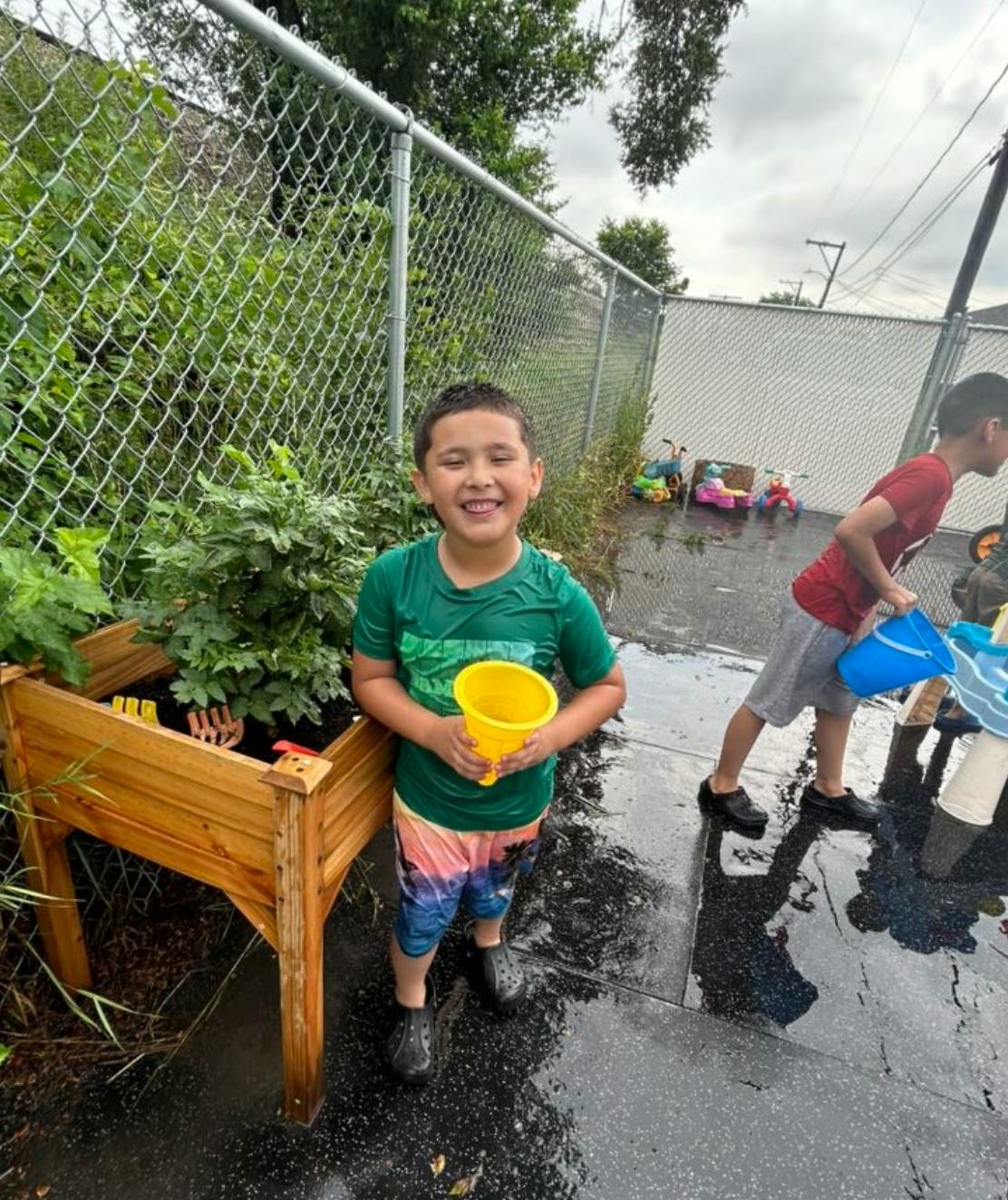 Child holding a yellow bucket next to a garden bed