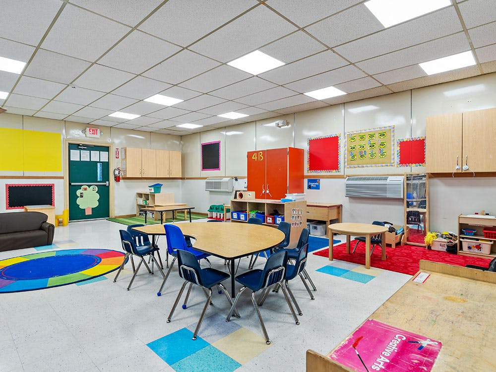 Classroom with tables, chairs, colorful rugs, and cabinets
