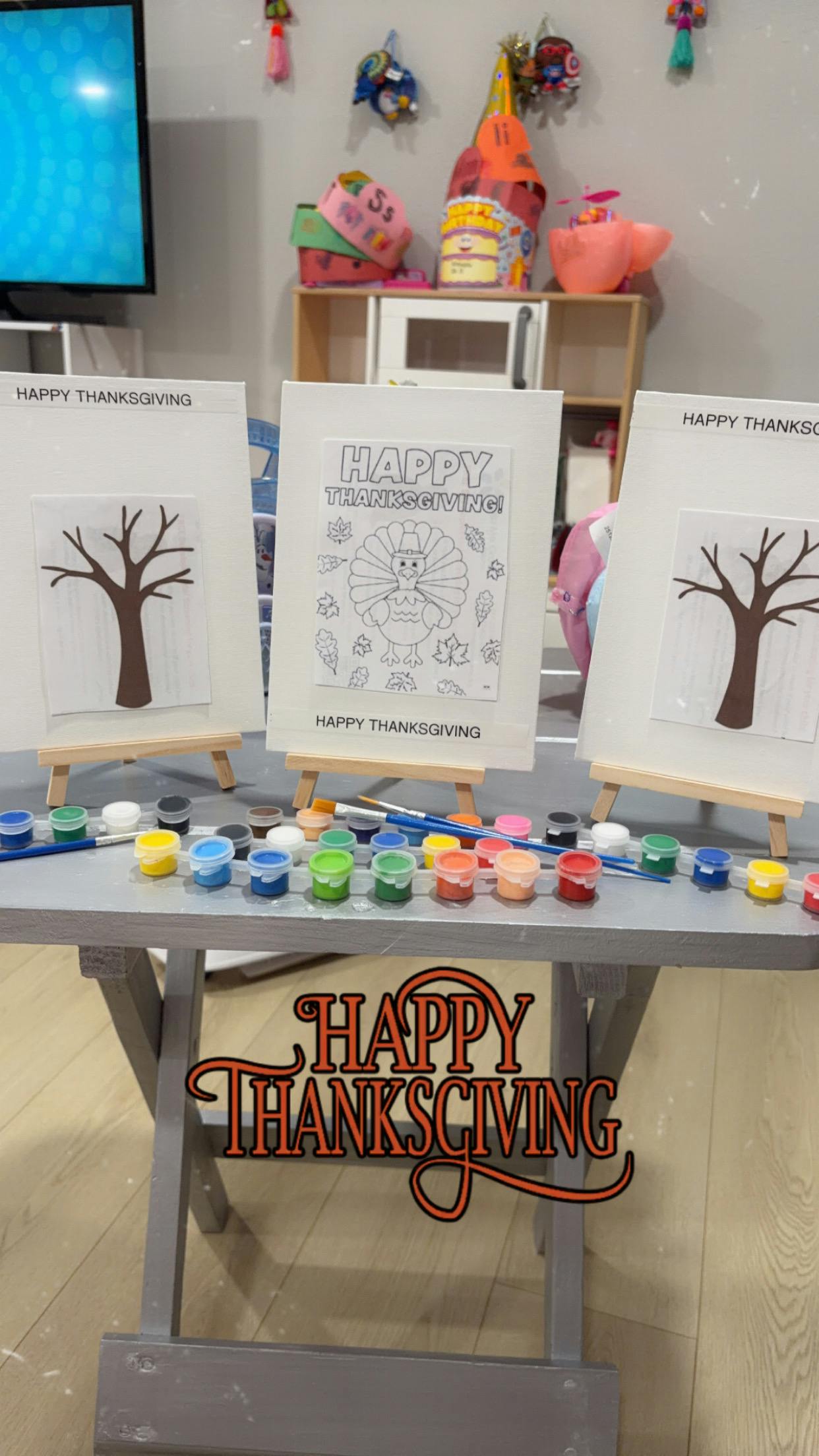 Art easels with tree paintings and a turkey coloring page, paint pots, and brushes