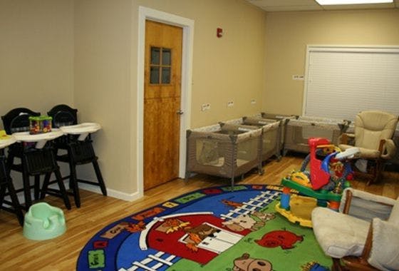 Room with cribs, high chairs, and a colorful play rug