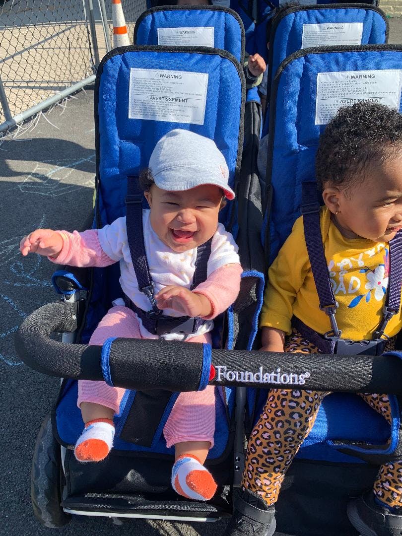 Two children in a multi-seat stroller, one wearing a hat and smiling