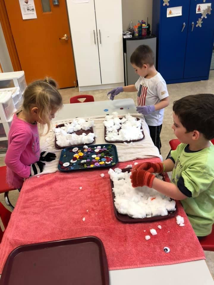 Three children playing with white foam and small objects at a table