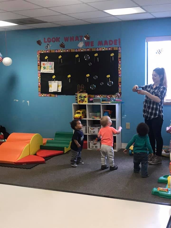 Person blowing bubbles for three children in a classroom