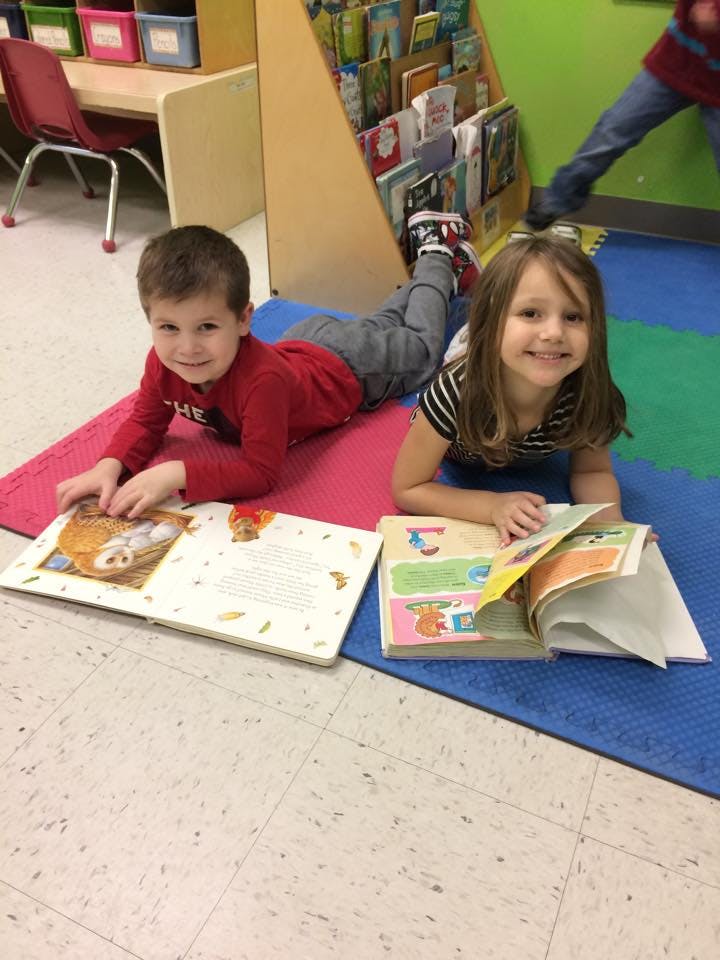 Two children lying on mats reading books in a classroom