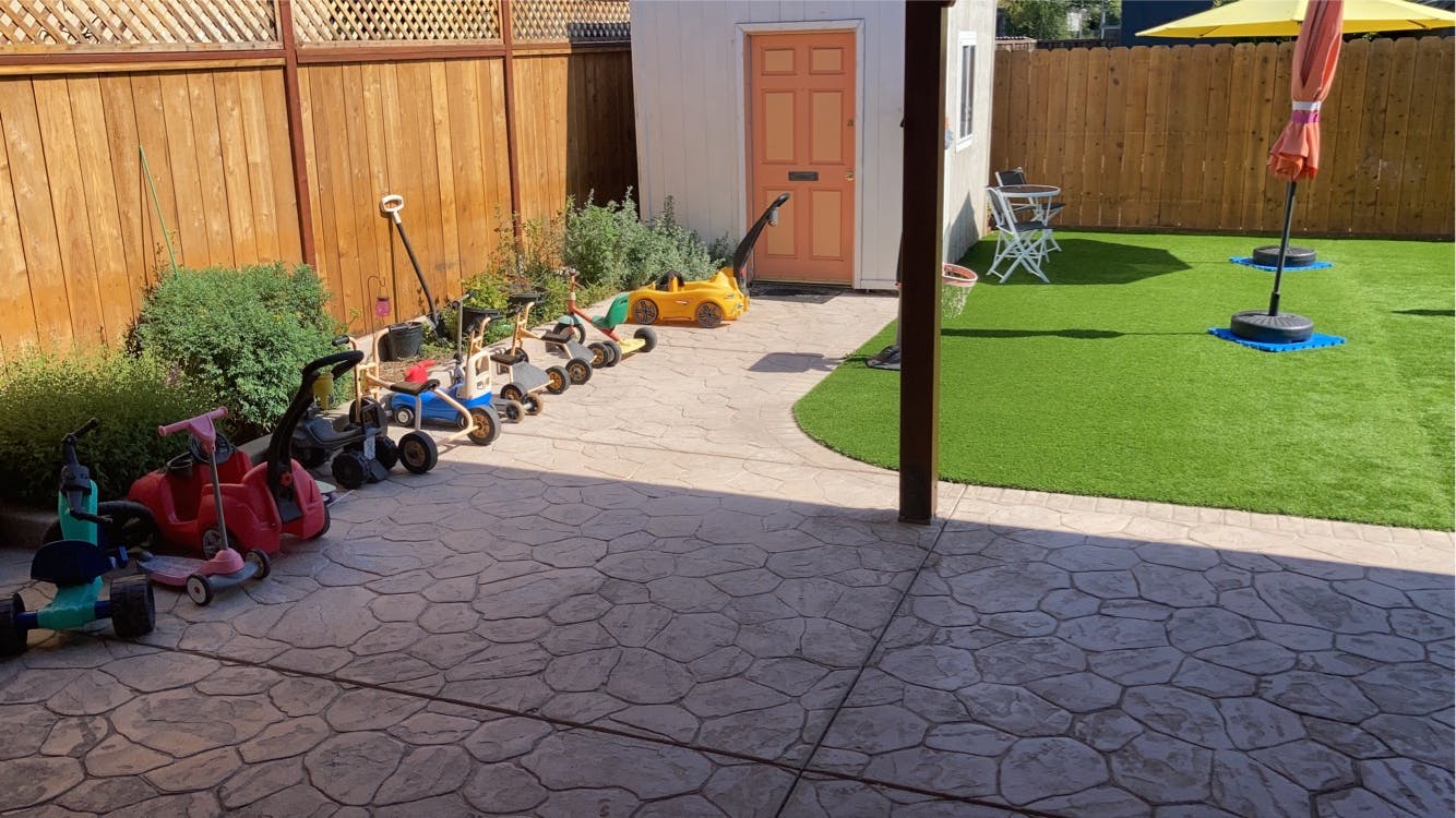 Backyard with artificial turf, patio, and children's ride-on toys