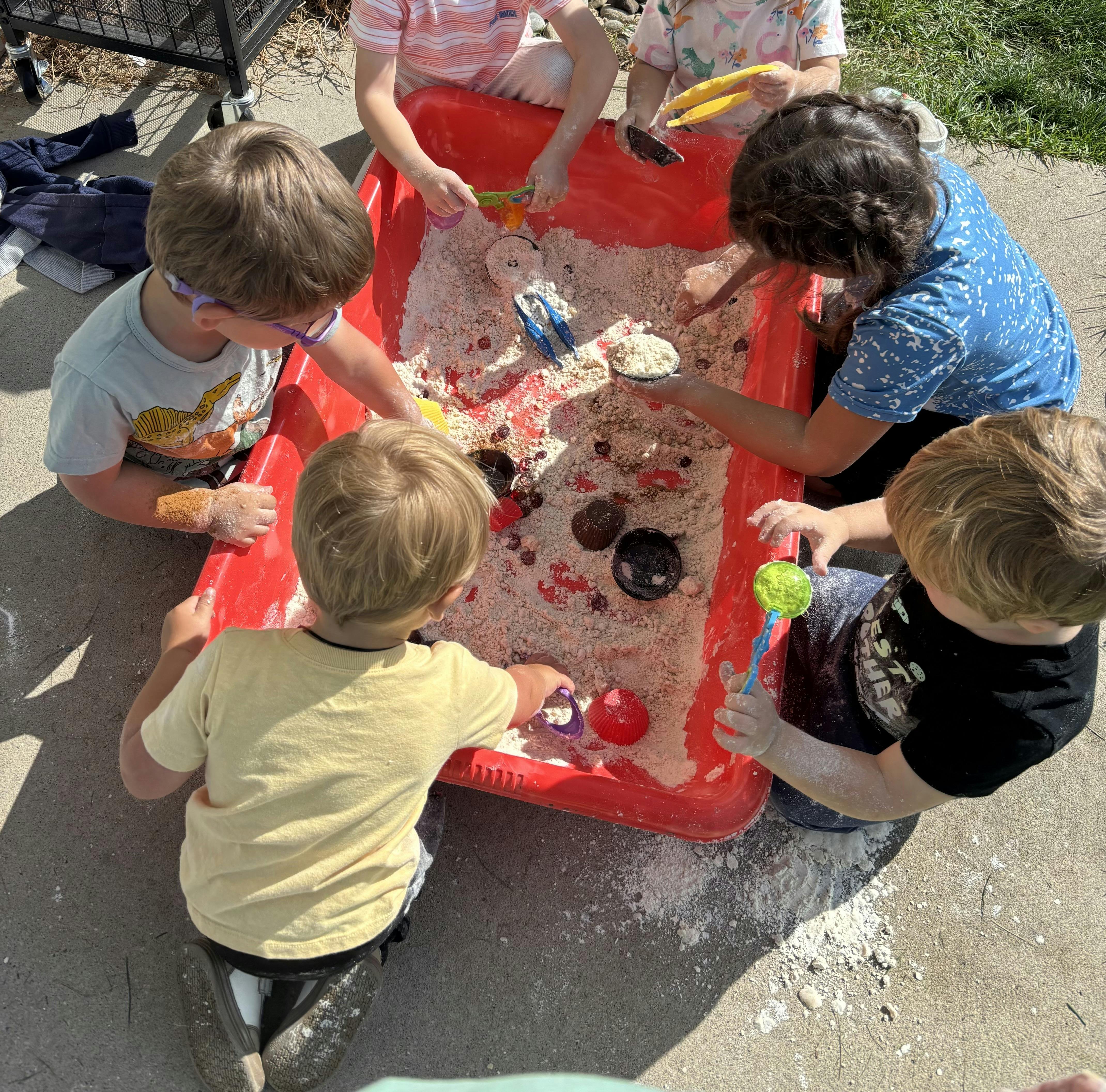 Children playing in a red sensory bin with sand and toys