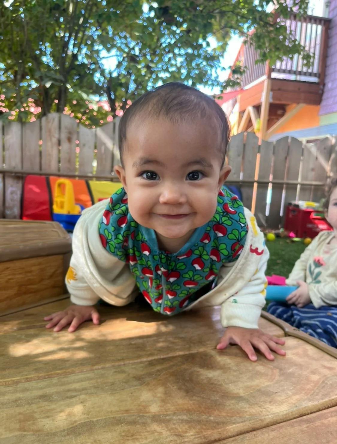 Child smiling and crawling on a wooden surface outdoors