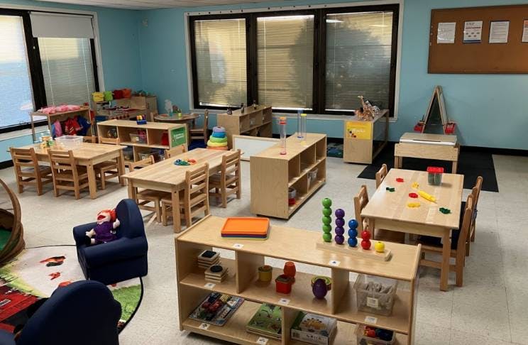 Classroom with small wooden tables, chairs, and shelves filled with toys and learning materials