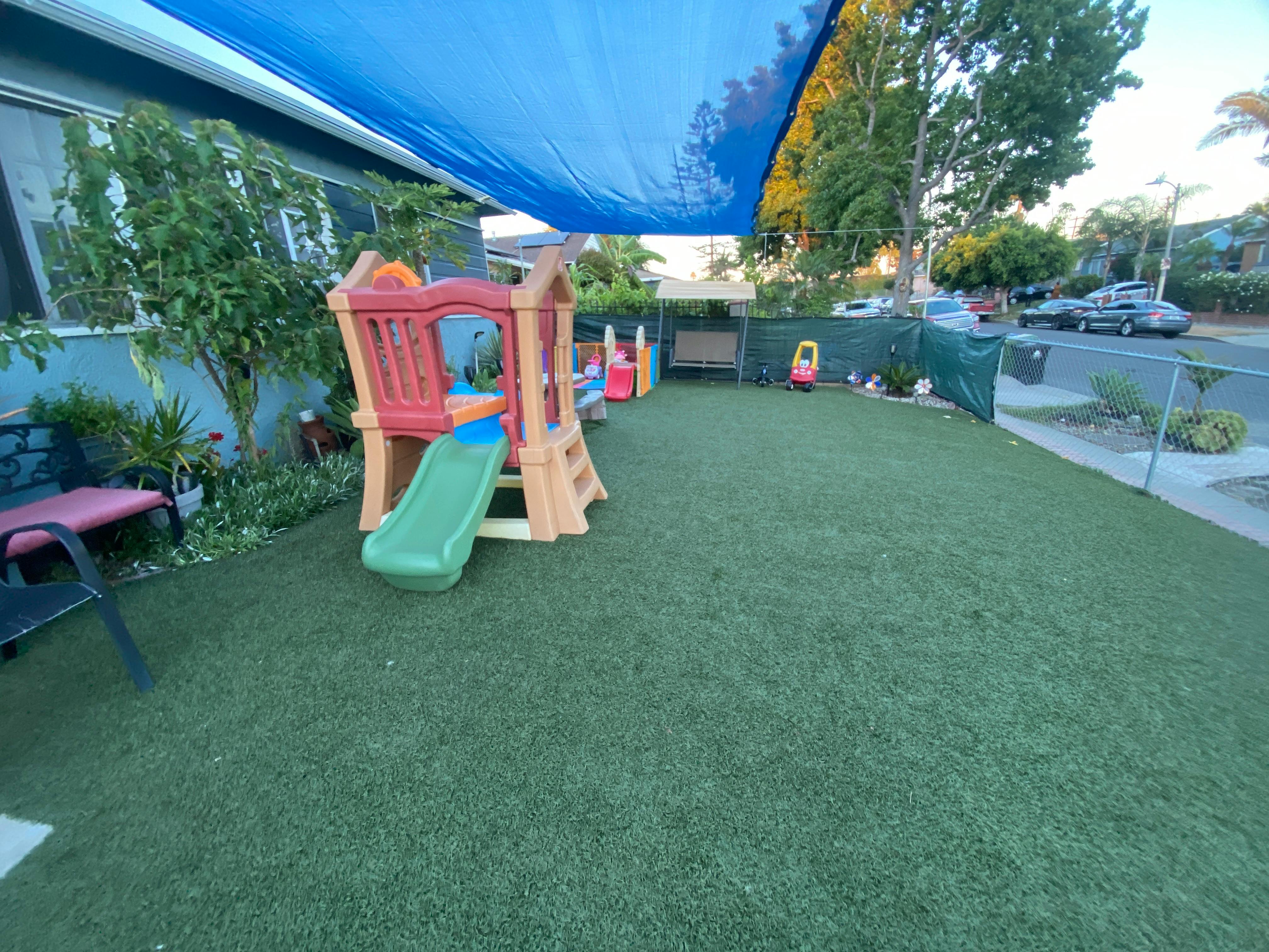 Playground with a slide and artificial turf under a blue shade