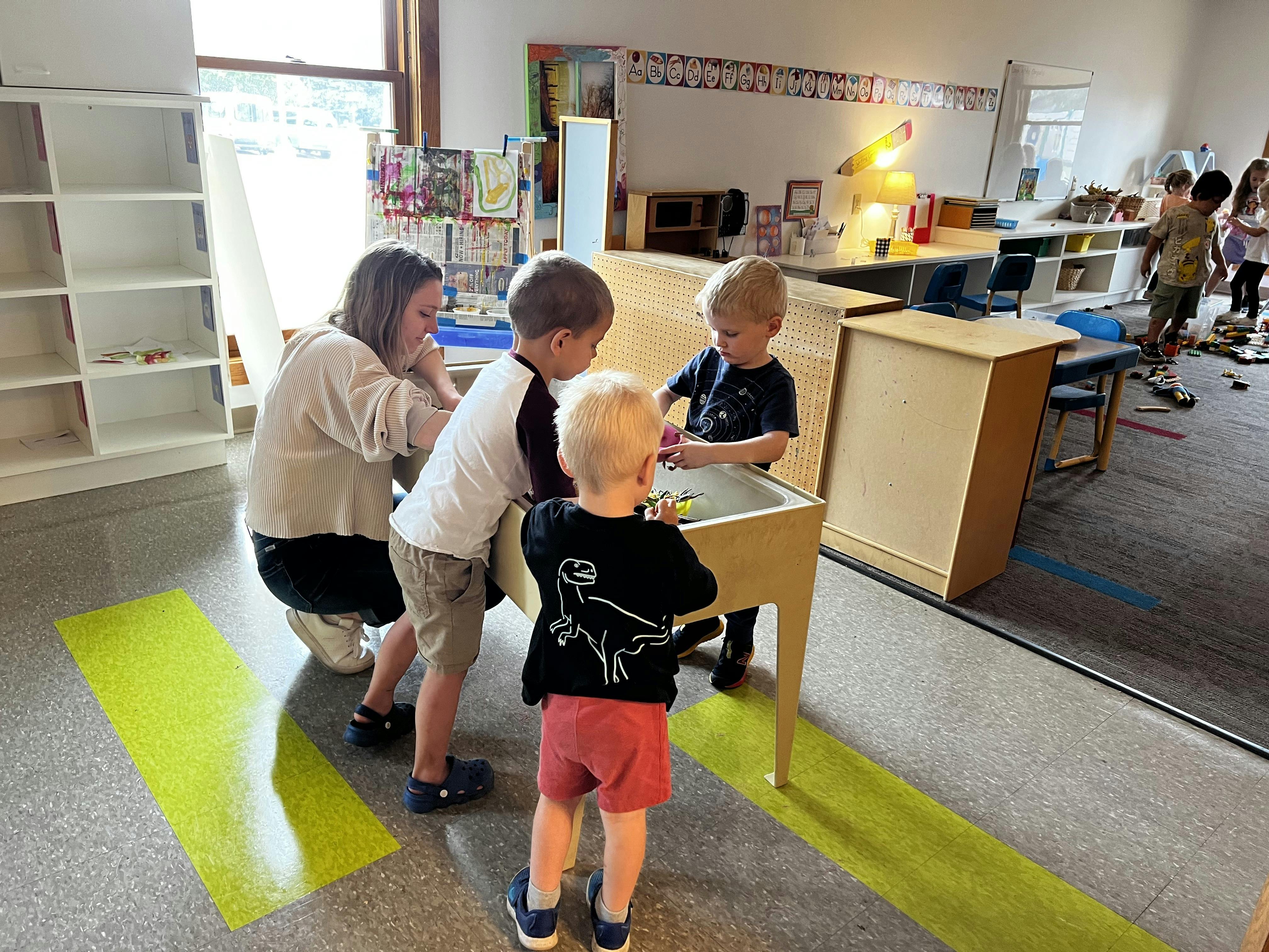 Adult and three children playing at a table in a classroom