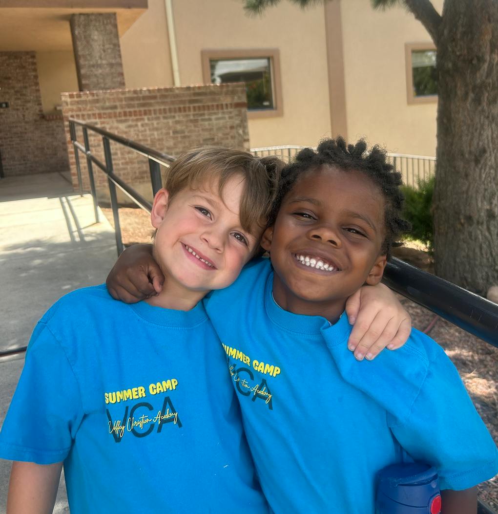 Two children in blue shirts with "Summer Camp VCA" text, one with arm around the other