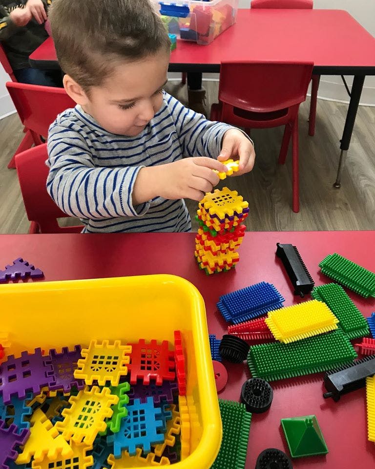 Child playing with colorful interlocking building blocks at a red table