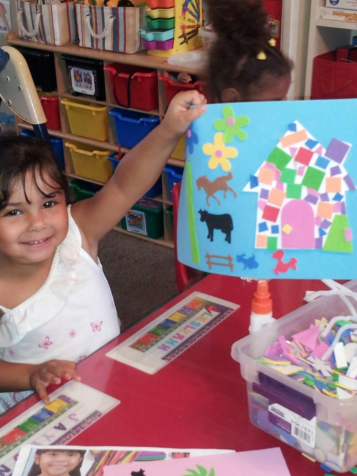 Child holding up a paper craft with a house and animals