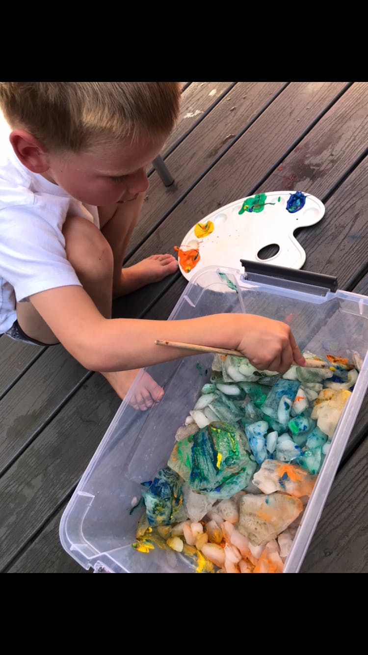 Child painting rocks in a clear container with a paintbrush