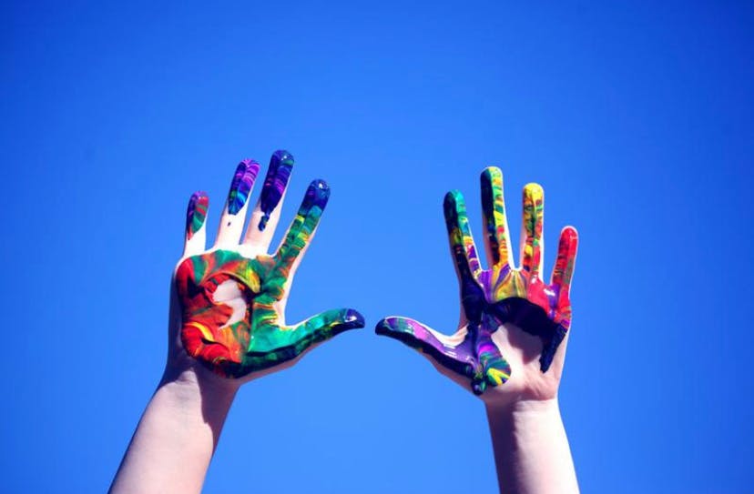 Two hands covered in colorful paint against a blue sky